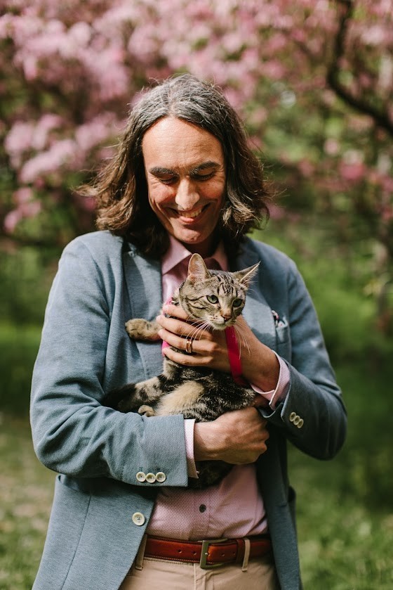 A photo of Geoff staring lovingly at his tabby cat as he holds it. He is dressed in his teaching attire.